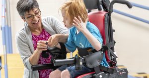 אשה עוזרת לילד לשלוט בכסא גלגלים